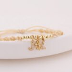 Pulsera De Oro 18K Con Esferas Esferas  Hilo Color Beige Dijes Letra J Y L Y Dije Tres Gracias